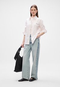 Svijetloružičasta košulja na dugmad, svijetloplave traperice visokog struka širokog kroja, crne ravne cipele sa čavlima i crna torba. Jednostavan, ležeran izgled.