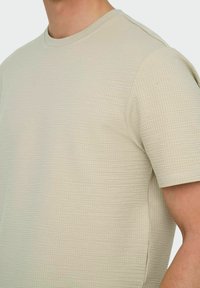 Lyse beige kortærmet T-shirt med et tekstureret, rutenet-lignende mønster og rund hals. Glat materiale med en skræddersyet pasform.