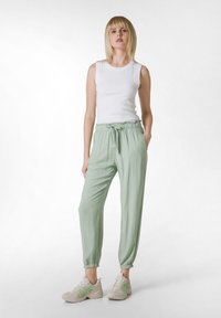 Pantalones jogger de color verde claro con cintura y puños elásticos, combinados con una camiseta sin mangas blanca y zapatillas beige con detalles en verde.