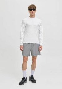 Vit långärmad skjorta, grå träningsshorts, svarta sportskor och svarta solglasögon. Enkel design, lättviktsmaterial, bekväm passform.