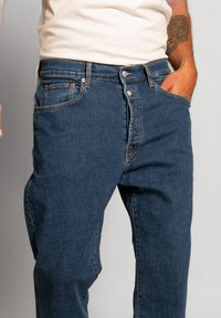 Jeans in denim di colore blu scuro con una vestibilità comoda. Le caratteristiche includono tasche anteriori e chiusura con bottone, con dettagli di cucitura in contrasto.