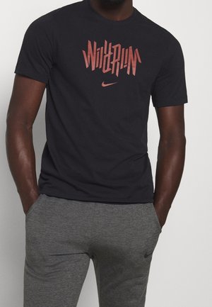 Camiseta de algodón negra con un gráfico angular rojo "Wild Run" y el logo de Nike. Combinada con unos pantalones de chándal en gris jaspeado con bolsillos laterales.