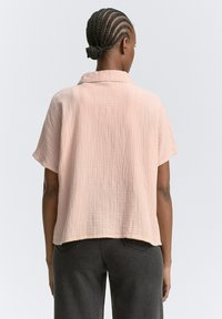 Maglietta a maniche corte di un morbido colore rosa con un tessuto testurizzato e leggermente stropicciato, abbinata a jeans grigi scuri.