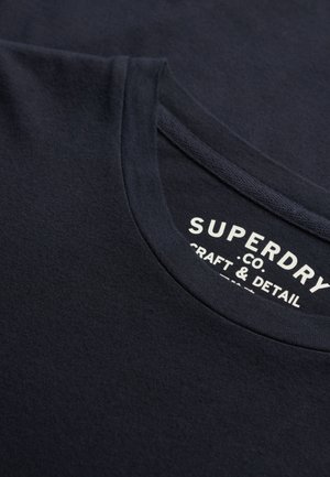 Navyblaue Baumwoll-T-Shirt mit Rundhalsausschnitt, glatter Textur und einem weißen Drucketikett mit "Superdry", "Craft & Detail."