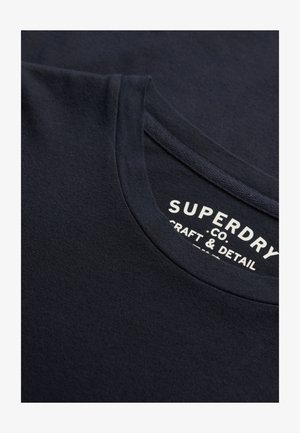 Navyblaue Baumwoll-T-Shirt mit Rundhalsausschnitt, glatter Textur und einem weißen Drucketikett mit "Superdry", "Craft & Detail."