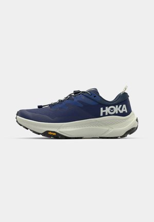 Scarpa da corsa HOKA di colore blu navy con tomaia in rete, suola intermedia spessa di colore crema, suola grigia, logo Vibram e lacci elastici per una chiusura rapida.