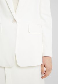 Blazer bianco con design strutturato, caratterizzato da una chiusura con un solo bottone, due tasche frontali e una texture del tessuto liscia.