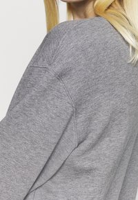 Sweatshirt gris en tissu texturé, avec une sensation douce, des épaules tombantes et une coupe décontractée. Design simple sans motifs ni accents.