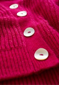 Fuchsian stickad tyg med stora, ovala gräddvita knappar med ett hål i mitten, som visar en texturerad ribbad design.