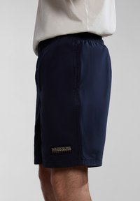Navy blue swim shorts with elastic waistband, side pockets, and a branded patch on the hem. Smooth fabric with a lightweight texture.