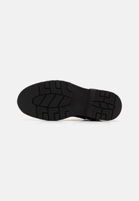 Suela de zapato de goma negra con un patrón de textura y acentos elevados, presentando un área central lisa y bordes redondeados.
