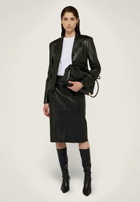 Svart läderblazer och pennkjol kombinerat med en vit topp, svarta knähöga stövlar och en svart handväska. Slät textur och åtsittande design.