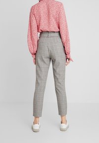 Höga grå rutiga byxor med en smal passform, med diskreta röda accenter. Matcher med en ljusröd blommig långärmad skjorta och vita sneakers.