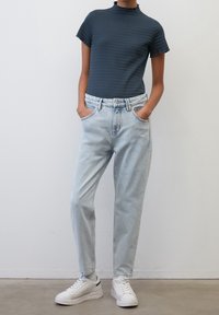 Přiléhavý tmavě modrý žebrovaný top s krátkým rukávem, který je spárován se světle modrými džíny s vysokým pasem a bílými teniskami. Hladká tkanina a volný střih.