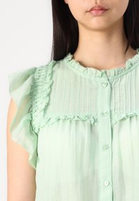 Blusa verde-menta com decote e mangas franzidas, riscas verticais e fecho frontal com botões. Tecido leve com textura suave.