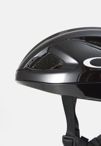 Czarny kask rowerowy z błyszczącym wykończeniem, aerodynamiczny kształt, otwory wentylacyjne i teksturowany akcent. Widoczny regulowany pasek.
