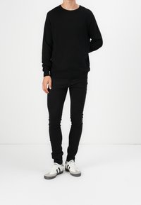 Black knitted crew-neck sweater, slim-fit black jeans, and gray/white sneakers with black stripes. Simple and clean design.