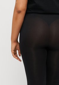 Black leggings with a smooth, stretchy material, featuring a high waist and a form-fitting design, accentuating the body's shape.