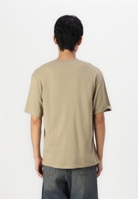 Short-sleeve, crew-neck t-shirt in khaki cotton. Features a relaxed fit with a smooth texture and straight hem. Back view shows simple design.