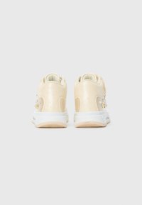 Een paar beige gestructureerde sneakers met witte zolen, bekeken vanuit de achterkant op een effen lichtgrijze achtergrond.
