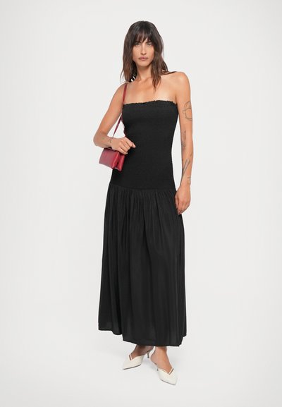 Rochie neagră fără bretele, cu un corset smockat și o fustă vaporoasă. Asortată cu o geantă roșie și mule albe cu vârful ascuțit.