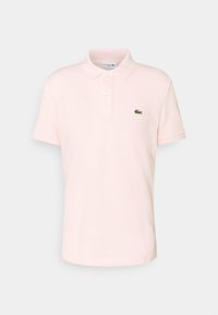 Camisa polo de manga corta en color rosa claro, con dos botones y un logo de cocodrilo verde en el lado izquierdo del pecho, sobre un fondo blanco.