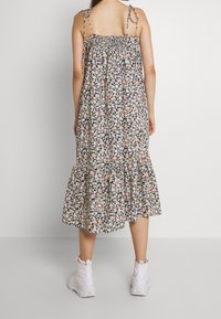 Blumiges Midikleid mit verstellbaren Spaghetti-Trägern, gerafftem Oberteil und gestuftem Rüschensaum. Buntes Blumenmuster auf schwarzem Hintergrund.