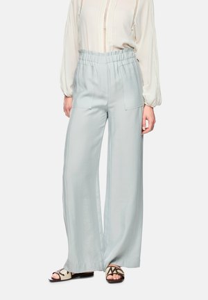 Woman wearing pale blue wide-leg pants with patch pockets and an elastic waistband, paired with cream blouse and open-toe sandals.