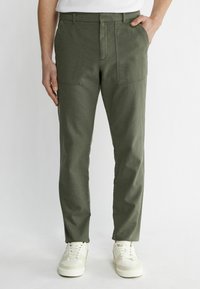 Kaki byxor med rak skärning, med två framfickor i patch-design och en jämn textur. Tillsammans med vita sneakers.