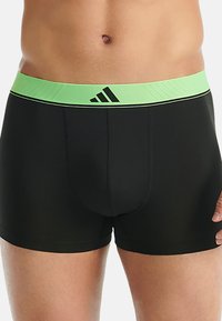 Černé boxerky s elastickým pasem v zelené barvě, zdobeným černým logem a pruhy. Hladká textura, přiléhavý střih.