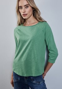 Vihreä, kevyt pitkähihainen paita, jossa on veneenkaula-aukko ja kolmanneksen mittaiset hihat; sileä rakenne ja rento istuvuus, jossa on hieman kiiltoa.