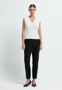 Top bianco senza maniche con scollo a V, tessuto testurizzato, vita aderente, abbinato a pantaloni neri su misura e tacchi a spillo neri.