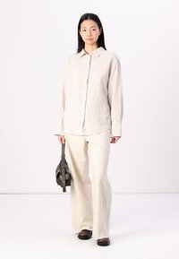 Gai bežs pogu krekls no lina ar garām piedurknēm, apvienots ar krēmkrāsas svārkiem ar platām apakšmalām un tumšām plakanām kurpēm, turot nelielu brūnu somu.