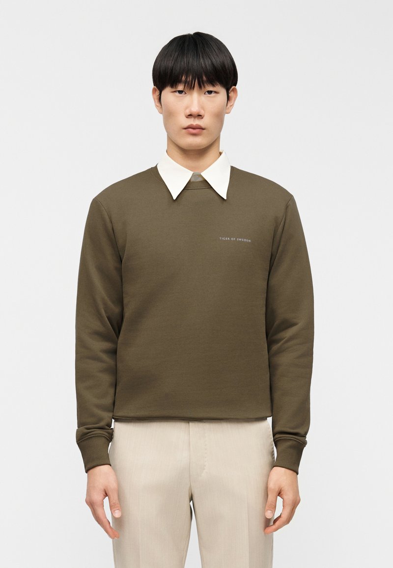 Ελιά πράσινο φούτερ με λευκό, δομημένο γιακά. Διαθέτει διακριτικό λογότυπο στο στήθος και ριμπ μανσέτες. Ομαλή υφή υφάσματος.