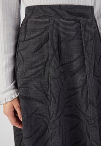Zwarte rok met textuurpatronen van bladeren, met een geweven fabricage ontwerp en subtiele roosterachtige accenten. Close-up weergave van de tailleband en plooien.