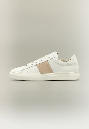 Pantof sport alb cu talpă joasă, dungă bej laterală, închidere cu șireturi și talpă plată din cauciuc pe fundal neutru.