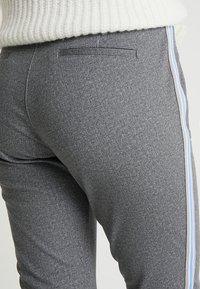 Pantalons gris à motif avec une texture lisse, présentant une bande latérale en bleu clair et un détail de poche arrière.