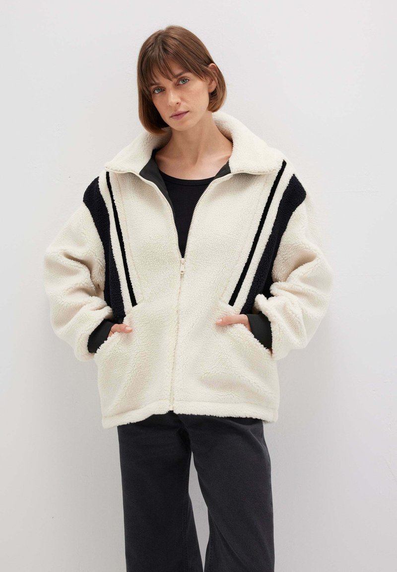 Fleece-Reißverschlussjacke in Creme mit schwarzen Streifen, mit hohem Kragen und seitlichen Taschen. Weicher Stoff und lässiger Schnitt.