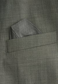 Grauer Anzugstoff mit einer strukturierten Webart, versehen mit einem gefalteten Einstecktuch in Grau mit einem geometrischen Rautenmuster.