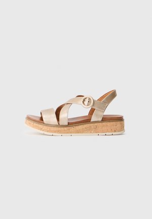 Sandale compensée dorée métallisée avec des brides croisées et une boucle circulaire, dotée d'une semelle intermédiaire en texture liège et d'une semelle en caoutchouc blanche.