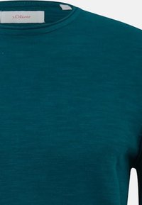 Maglione teal a girocollo realizzato in morbido tessuto testurizzato, con orlo cucito e un piccolo etichetta con il nome del marchio sul collo.