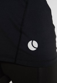 Mustat urheilushortsit, jotka on valmistettu joustavasta kankaasta, joissa on valkoinen logo ja näkyviä ompelutietoja. Läheinen näkymä korostaa kankaan rakennetta.