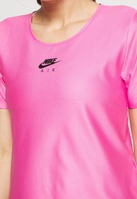 Camiseta deportiva de manga corta en color rosa, hecha de una tela texturizada y transpirable, con un logo negro de Nike Air en el centro.