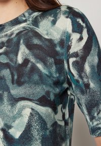 Stickad tröja med abstrakta mönster i teal, svart och crème. Rund halsringning, korta ärmar och texturerad yta.