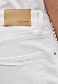 Λευκό τζιν από denim με υφή και ραμμένο σχέδιο, καθώς και ταμπέλα από δέρμα σε καφέ χρώμα με ανάγλυφο το λογότυπο "Pepe Jeans London". Κοντινή εικόνα της πίσω τσέπης.