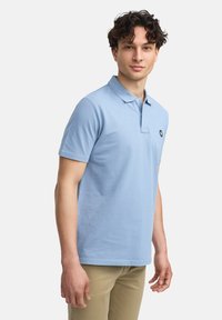 Lyseblå polo-shirt med klassisk krave, korte ermer og en liten logo på venstre bryst. Laget av myk, teksturert bomullstoff.