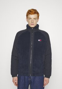 Giacca zip-up di colore navy con parte frontale in pile, maniche imbottite a contrasto, colletto alto e piccolo logo ricamato sul petto sinistro.
