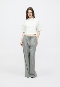 Camiseta blanca recortada con mangas enrolladas, combinada con pantalones de talle alto gris claro con cintura ajustable y diseño de pierna ancha.