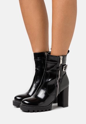 Bottines en cuir verni noir avec un talon épais, fermetures éclair et un détail de boucle latérale. Semelle extérieure texturée pour une meilleure adhérence.