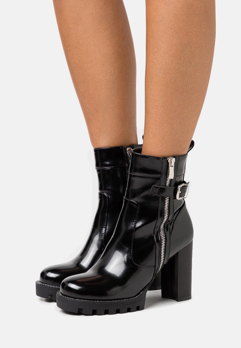 Bottines en cuir verni noir avec un talon épais, fermetures éclair et un détail de boucle latérale. Semelle extérieure texturée pour une meilleure adhérence.